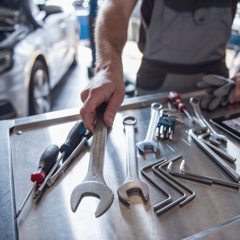 Cropped image of handsome young auto mechanic in uniform choosing tools for repairing car in auto service
