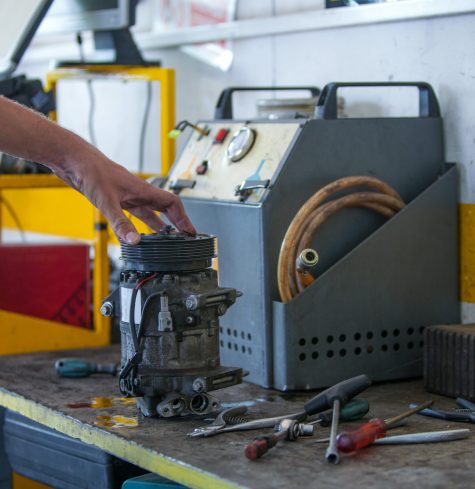 A caucasian male holding a damaged part of a car next to his working tools