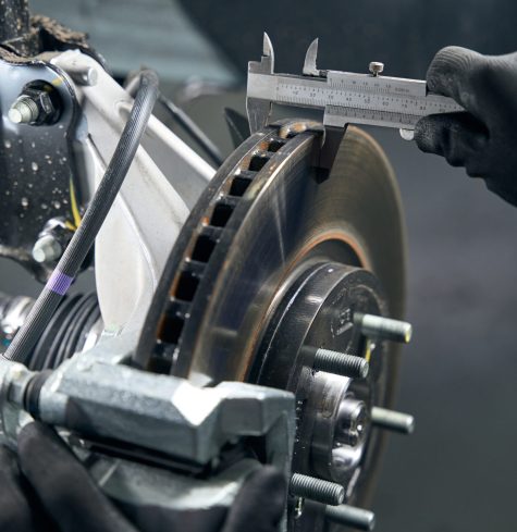 Man in protective gloves standing in tire fitting near car and checking brake drum wear