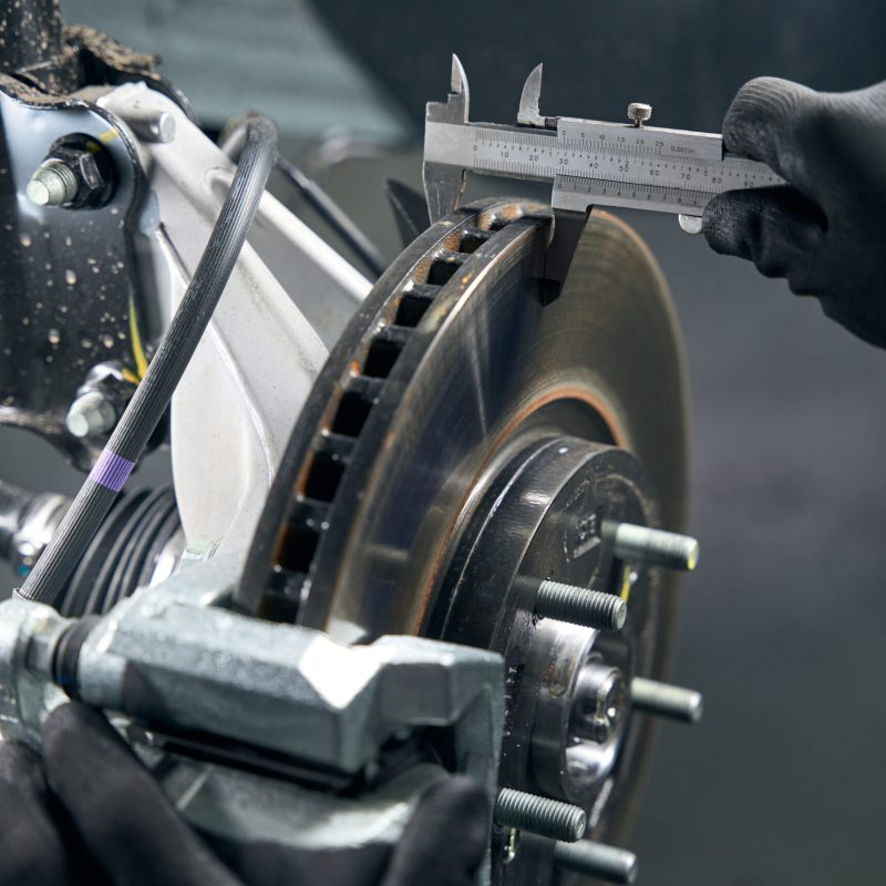 Man in protective gloves standing in tire fitting near car and checking brake drum wear