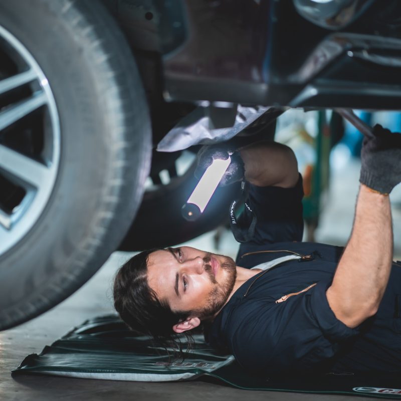closeup professional machanic portrait photo wearing uniform, Using a ratchet underneath the car maintenance, working concept.