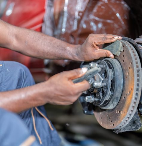Mechanical man sitting concentrate use wrench to repair car front tire drum brake pad at the car repair shop