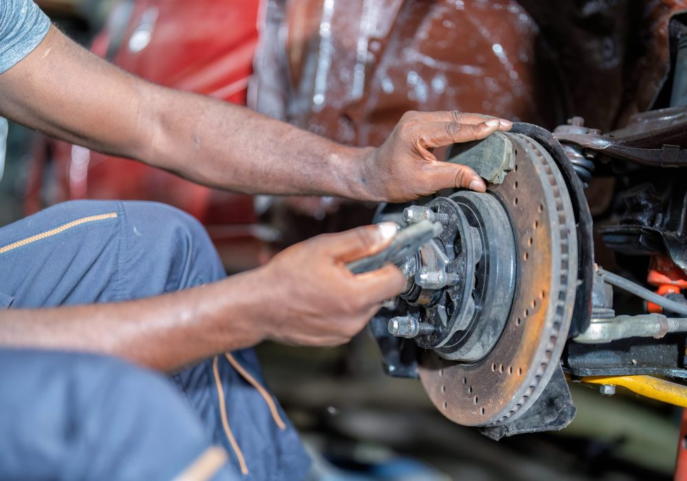 Mechanical man sitting concentrate use wrench to repair car front tire drum brake pad at the car repair shop