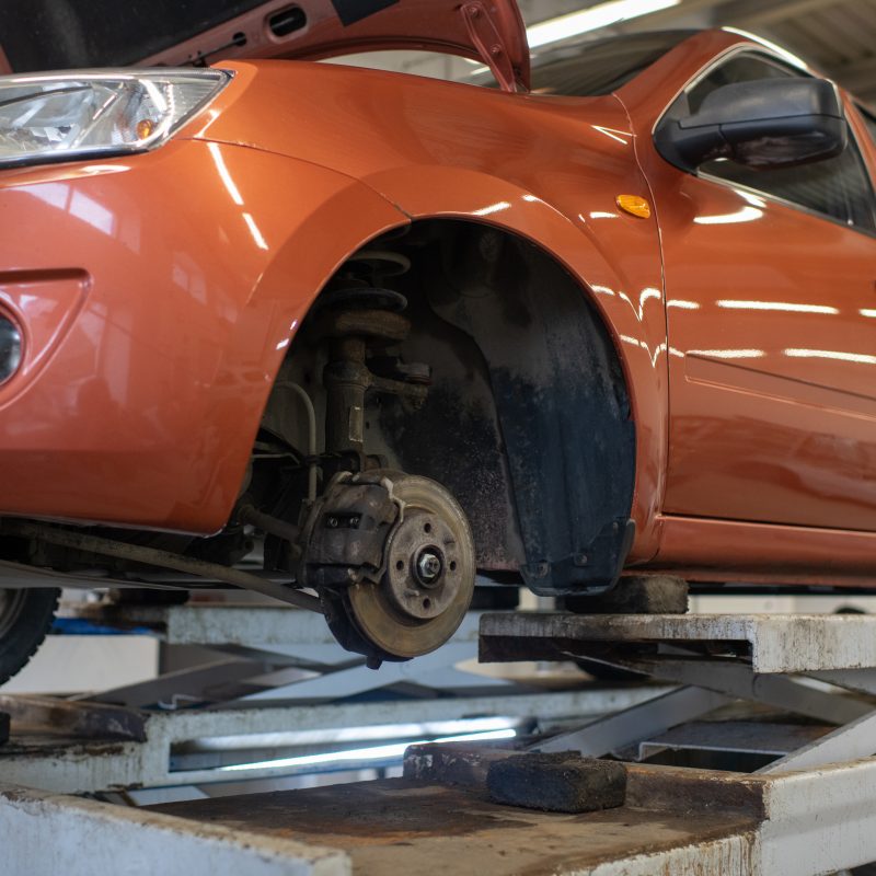 Side part of broken car of light brown color without one wheel standing in workshop to get checked and repaired