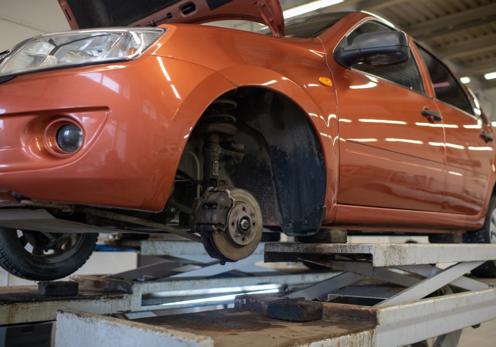 Side part of broken car of light brown color without one wheel standing in workshop to get checked and repaired